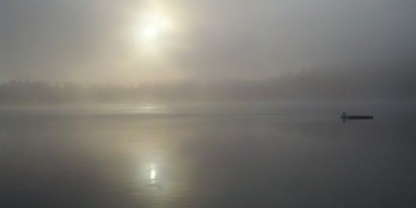 Sun shining through fog over a calm lake with a small dock. Mindfulness and Meditation go hand in hand with time spent outdoors. It is natures Therapy and a path to mental health.