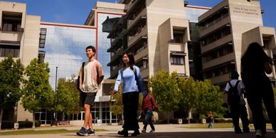 Students walking outside a university building on a sunny day.