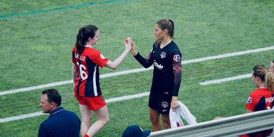 Two female soccer players sharing a handshake on the field.