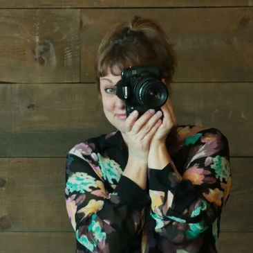 Woman in floral blouse taking a photo with a camera.