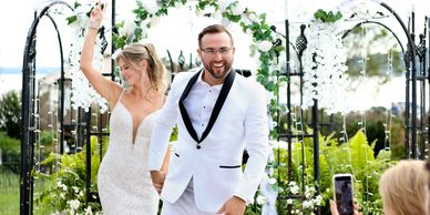 Happy bride and groom celebrating under floral arch at outdoor wedding.