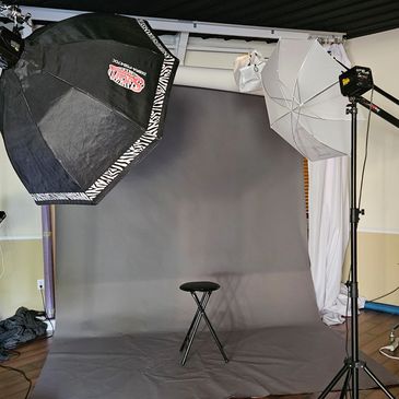 Photography studio setup with lighting and a stool against a gray backdrop.