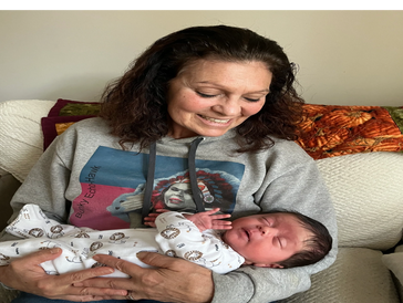 A smiling woman holds a peacefully sleeping newborn baby.