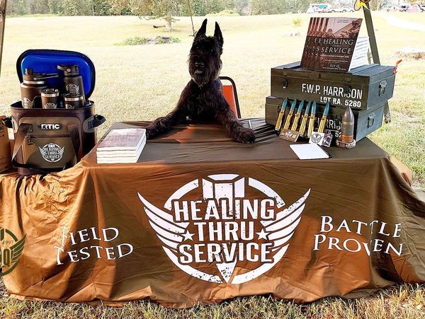 Healing from mental health trauma by serving others. Black dog sitting at a table selling a book.