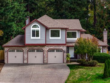 A large two-story house with a three-car garage surrounded by greenery.