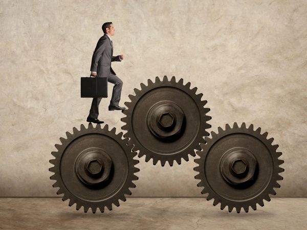 Businessman stepping on interconnected gears symbolizing progress.
