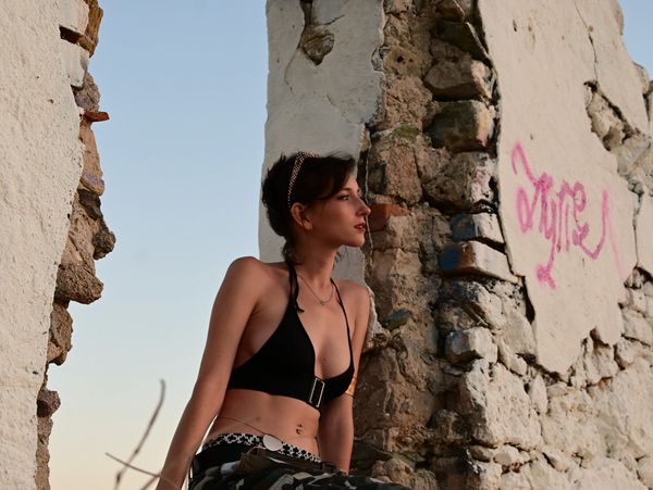 Young woman in black top sitting by a weathered stone wall with graffiti.