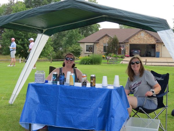 Two women sitting at a blue-covered table under a canopy outdoors.