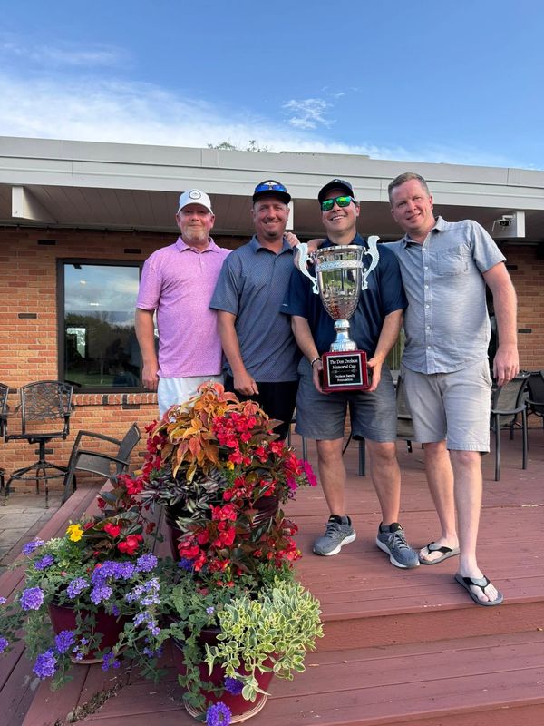 Four men standing on a deck holding a cup style large trophy.