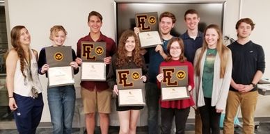 High school students holding folders that display their varsity letter and patch for volunteerism.