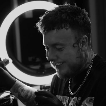 Man smiling while getting a tattoo with a ring light behind.