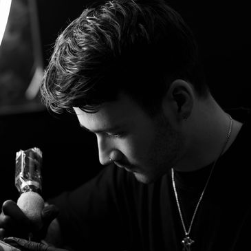 Black and white close-up of a focused man tattooing with a machine.