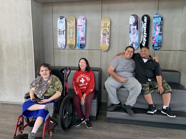 Four friends sitting indoors with skateboards on the wall.