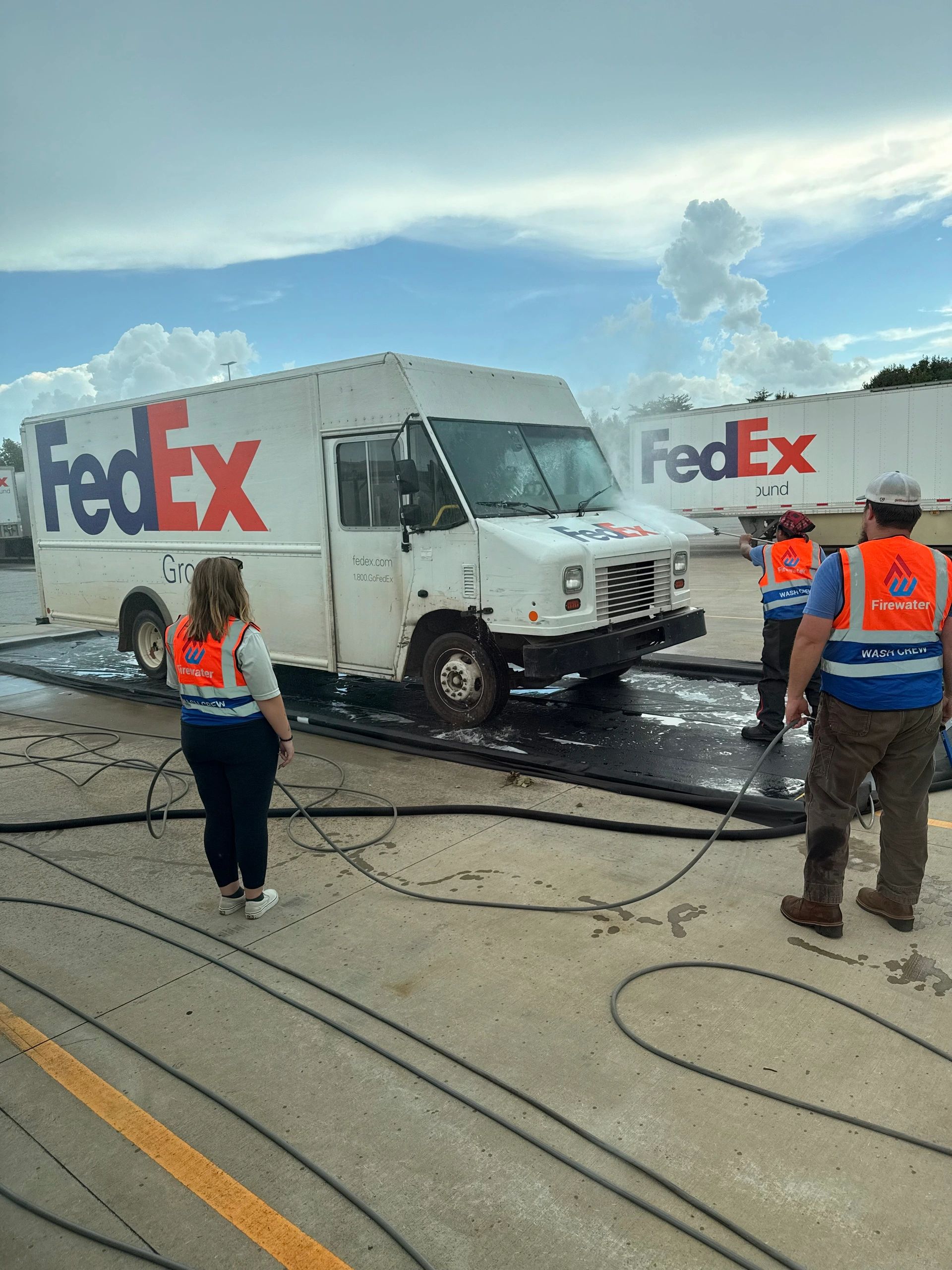 Workers washing a FedEx delivery truck outdoors.