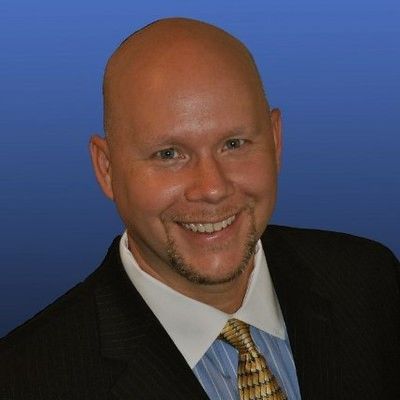 Smiling bald man in a suit with a blue background.