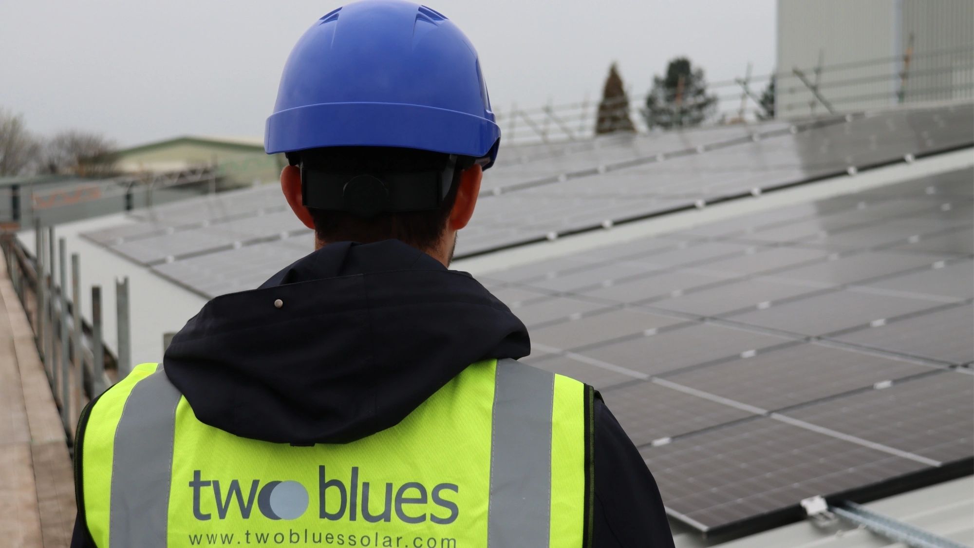 Worker in safety gear inspects solar panels on a rooftop.