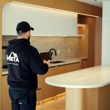 A man in a black hoodie inspects a modern kitchen with wooden cabinets and a marble island.