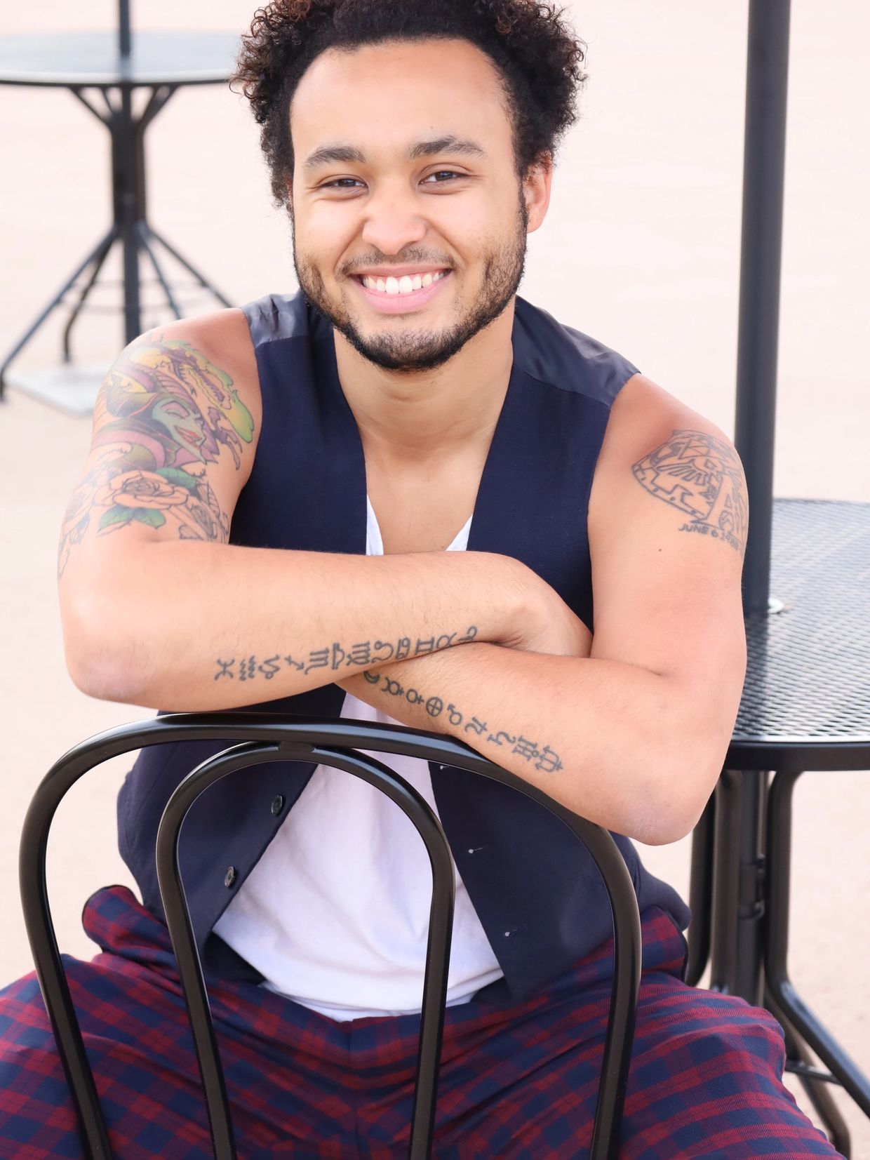Smiling young man with tattoos on arms sitting on a chair outdoors.