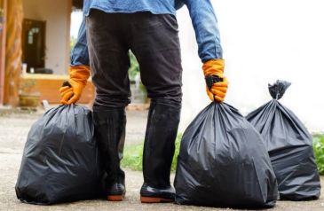 Person carrying two large black garbage bags outdoors.