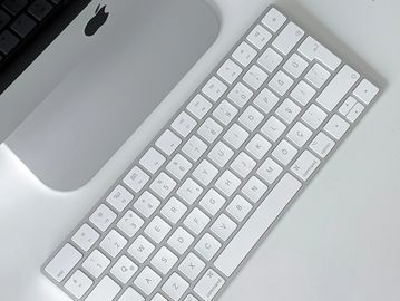 Apple wireless keyboard on a white desk next to an iMac.