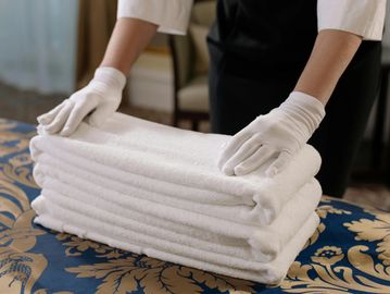 Person wearing white gloves arranging folded white towels on a patterned table.