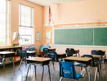 Empty classroom with desks, chairs, and a chalkboard under soft daylight.