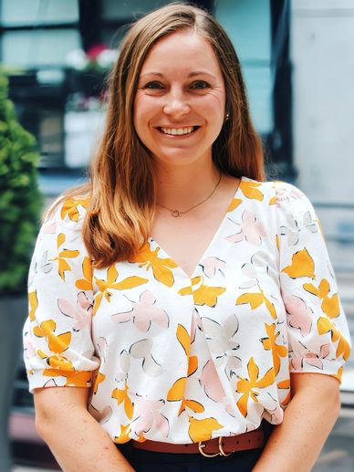 Smiling woman wearing a floral blouse with yellow and pink patterns.