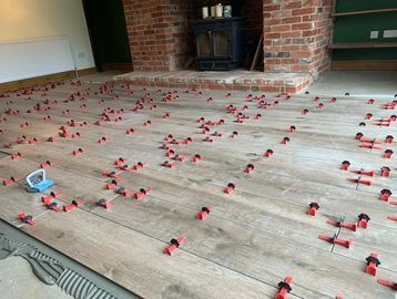 Wooden floor tiles being installed with spacers and leveling clips.