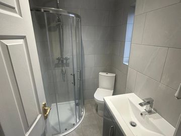 Modern small bathroom with glass shower, toilet, and sink vanity.