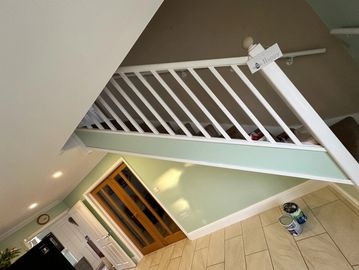 Indoor staircase with white railing and paint cans on tiled floor.