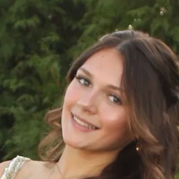 Young woman smiling outdoors with greenery background.