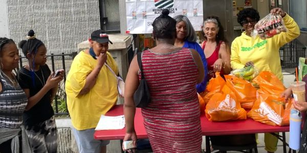 People gathered around a table with orange bags and fresh produce.