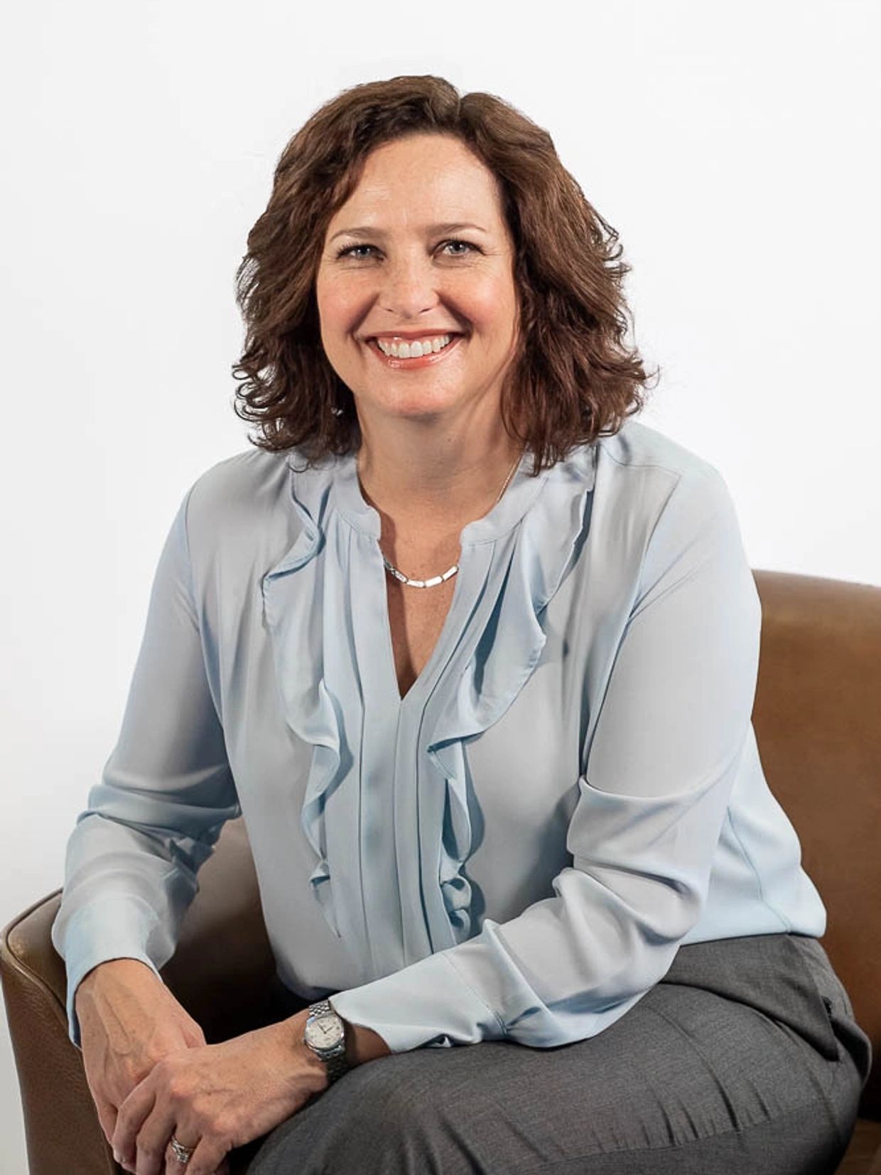 Wendy Ryan sitting on a brown leather chair in front of a white background