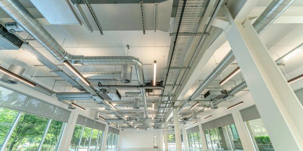 Modern industrial ceiling with exposed ductwork and lighting in a bright room.