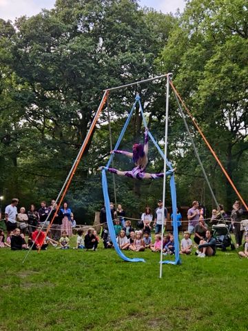 Aerial silk artist performs a split suspended in the air outdoors.