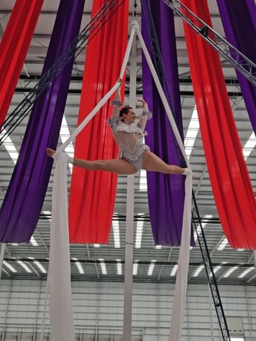 Aerial silk performer in mid-split leap with red and purple drapes.