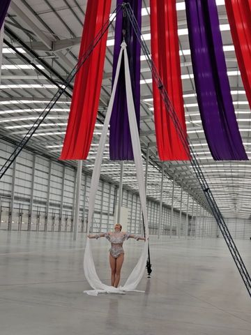 Aerial silk performer in a large industrial space with red and purple fabric.