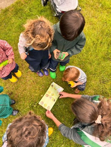 Children gathered around looking at a book outdoors.