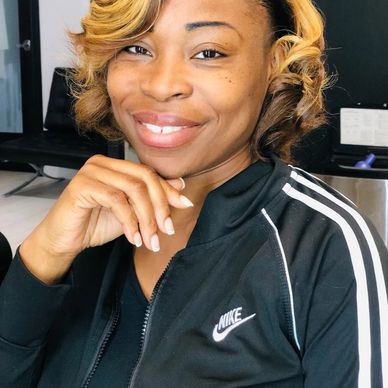 Smiling woman with styled blonde curls in a black Nike jacket.