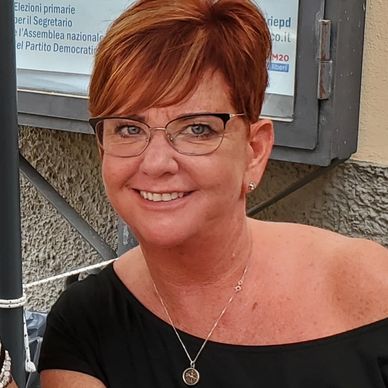 Smiling woman with glasses and short red hair wearing a black top.