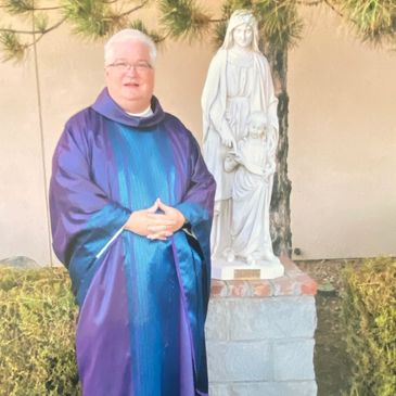 Clergyman in purple robe standing beside a statue of a woman and child.