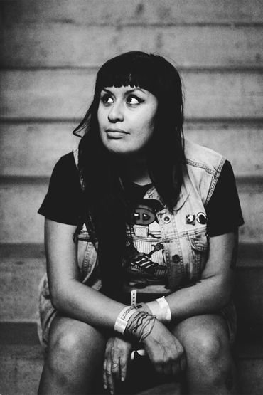 black and white photo of a woman sitting on concrete steps. She has black hair with bangs and is wea