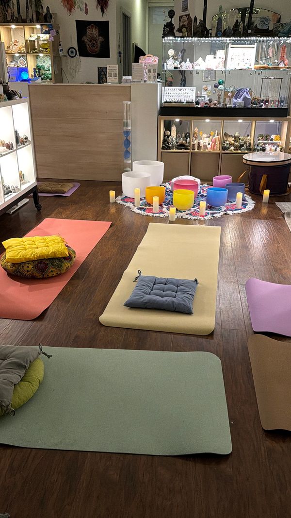 Yoga mats and cushions arranged around colorful singing bowls and candles in a serene room.