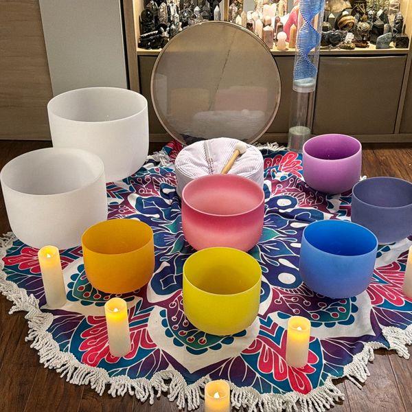 Colorful crystal singing bowls and candles arranged on a patterned cloth for meditation.