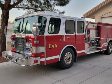 Red and white fire truck parked on a driveway near a tree and house.