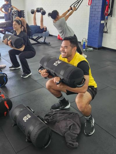 People working out in a gym using weighted bags and dumbbells.