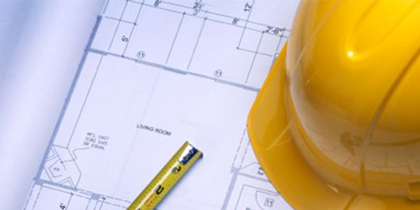 Yellow construction helmet and tape measure on architectural blueprints.
