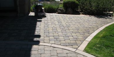 A paved stone driveway with a curved edge and lawn beside it.
