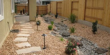 A backyard with a stone pathway and a dry riverbed landscape design.