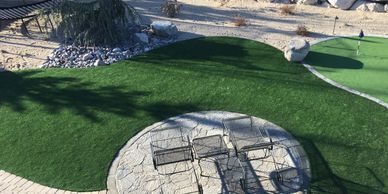 Small stone patio with chairs on green lawn under sunlight.